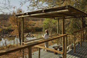 A wooden deck with a pergola, overlooking a body of water and a forested area.