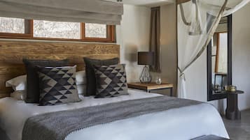 Een slaapkamer met een groot bed, een nachtkastje met een lamp, een raam met gordijnen en uitzicht op bomen.