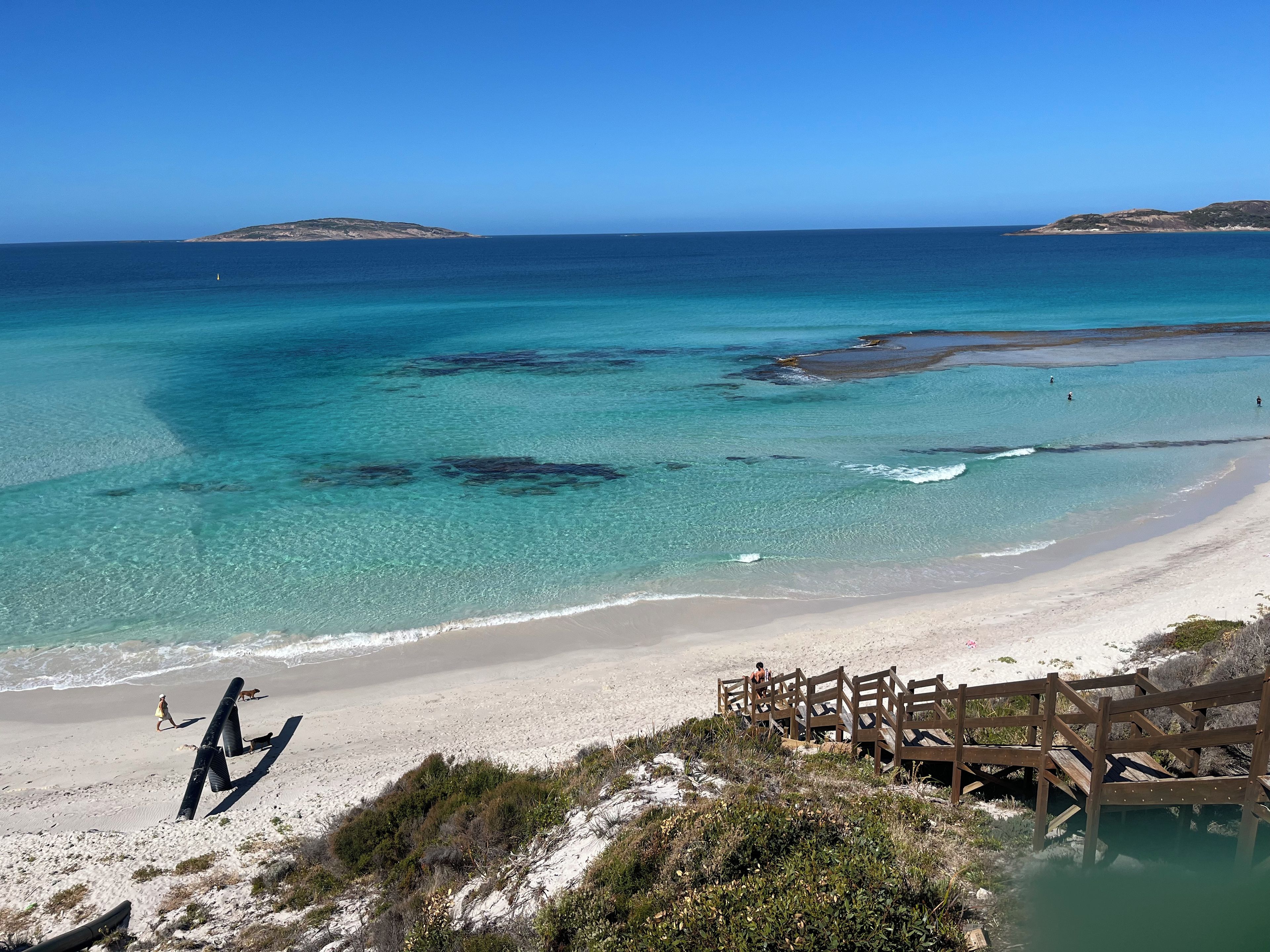 A beach with clear turquoise waters, a sandy shore, and a wooden boardwalk leading to a small wooden structure.