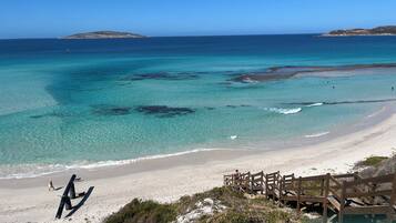 A beach with clear turquoise waters, a sandy shore, and a wooden boardwalk leading to a small wooden structure.
