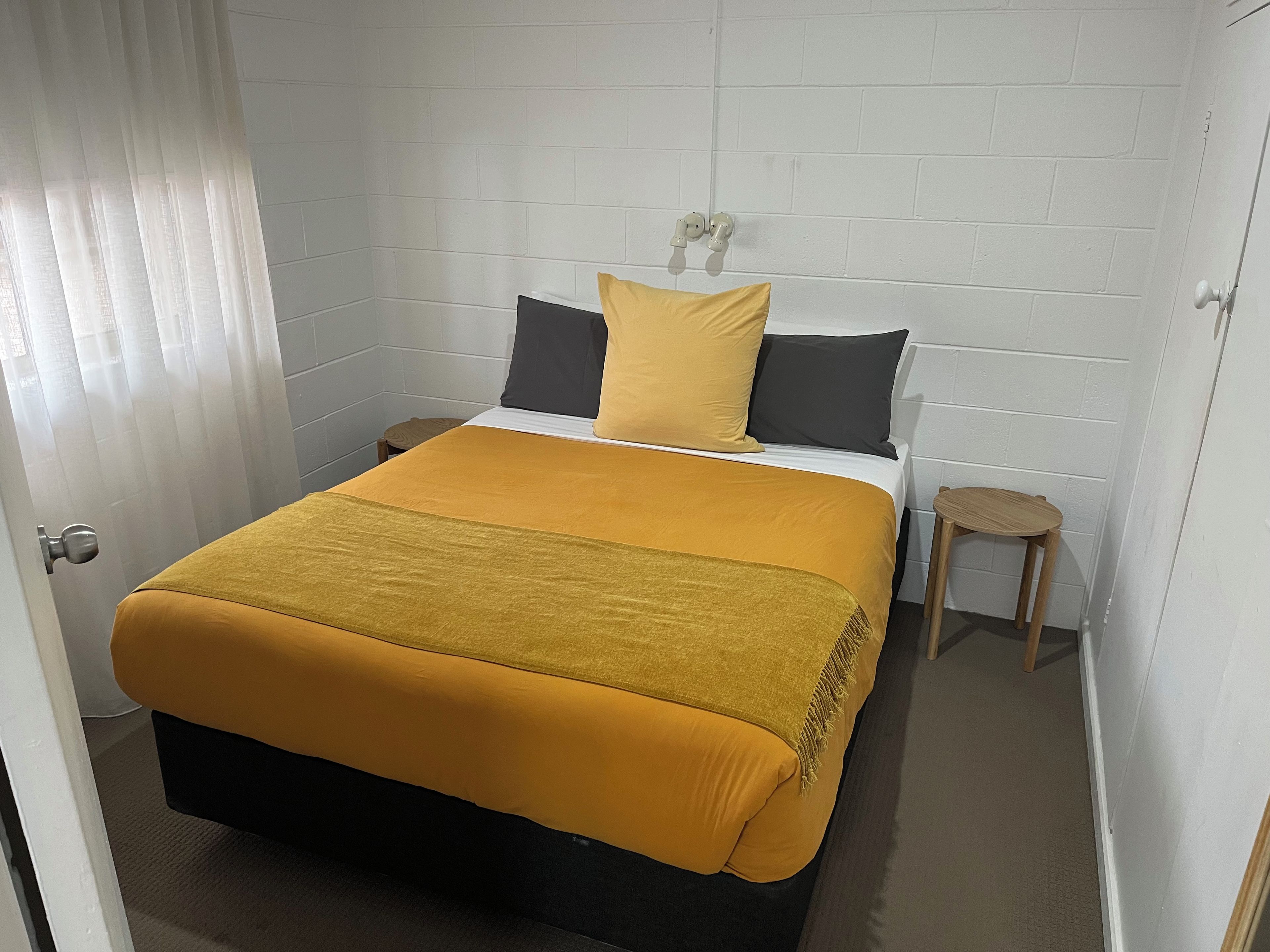 Un dormitorio con cama, mesitas de noche, un taburete pequeño y una pared de ladrillo blanco.
