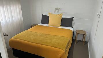 Un dormitorio con cama, mesitas de noche, un taburete pequeño y una pared de ladrillo blanco.