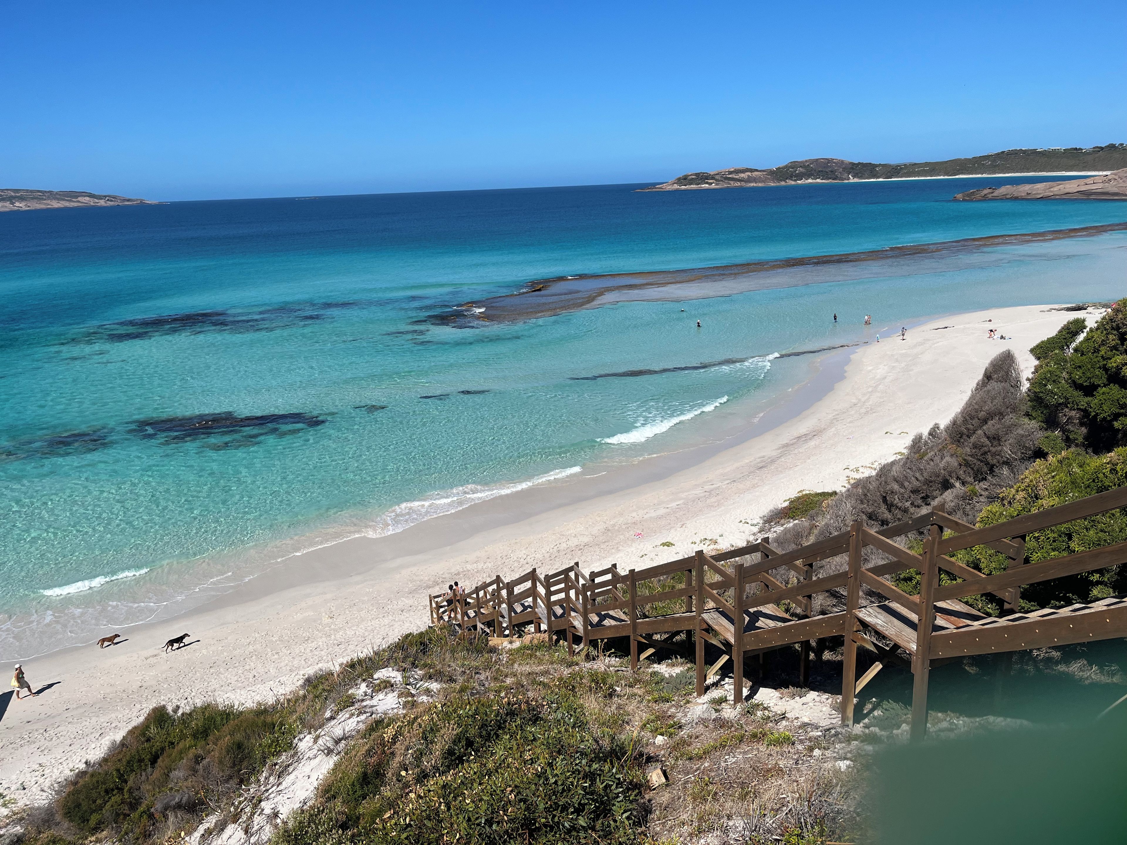 A beach with clear turquoise waters, a sandy shore, and a wooden staircase leading down to the beach.