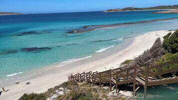 A beach with clear turquoise waters, a sandy shore, and a wooden staircase leading down to the beach.
