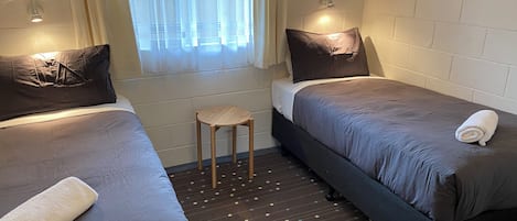 A room with two beds, a small stool, and a window with curtains.