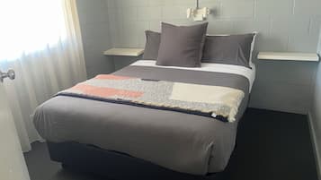 A bed with a grey blanket, two pillows, and a bedside table with a lamp.