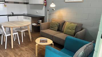 A compact living space with a kitchenette, a sofa, a small table, and a blue armchair.