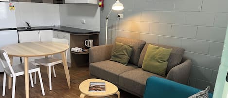 A compact living space with a kitchenette, a sofa, a small table, and a blue armchair.