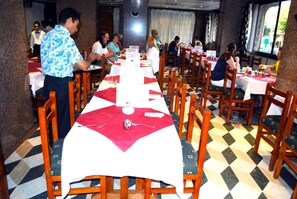 A restaurant with multiple tables and chairs, a checkered floor, and a waiter serving. - Stjosephhotel (Luxor)