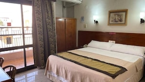 Ein Hotelzimmer mit Bett, Schreibtisch, Stuhl, Kleiderschrank, Klimaanlage und Blick durch eine Schiebetür.
