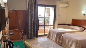 Ein Hotelzimmer mit einem Bett, einem Schreibtisch mit Wasserkocher, einem Sessel, einem Fenster mit Vorhängen und einer Klimaanlage.