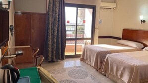 Ein Hotelzimmer mit zwei Betten, einem Schreibtisch mit Stuhl, einem grünen Tisch und Blick ins Freie.