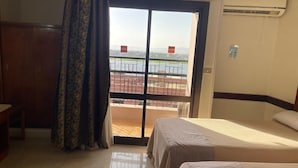 Ein Hotelzimmer mit Bett, Schreibtisch, Fenster mit Blick auf ein Gewässer und einer Klimaanlage.
