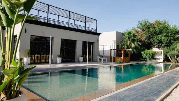 A modern pool area with a clear pool, a covered outdoor seating area, and lush greenery. - Palais Jena Hotel & Spa (Marrakech)
