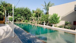 A swimming pool with a tiled edge, surrounded by greenery and a building with a flat facade. - Palais Jena Hotel & Spa (Marrakech)