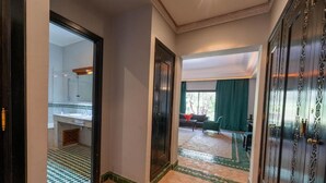 A hallway with a checkered floor pattern, a mirror reflecting a bathroom, and a door leading to a room with a green curtain. - Palais Jena Hotel & Spa (Marrakech)