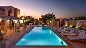 A swimming pool with lounge chairs and tables, surrounded by a building with a flat roof and a covered patio area. - Palais Jena Hotel & Spa (Marrakech)