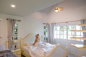 Ein Schlafzimmer mit einem Bett, Nachttischen, einem Fenster mit Vorhängen und einem Deckenventilator.