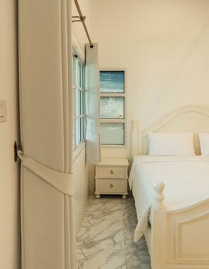 Un dormitorio con cama, mesita de noche, ventana con vistas y puerta.