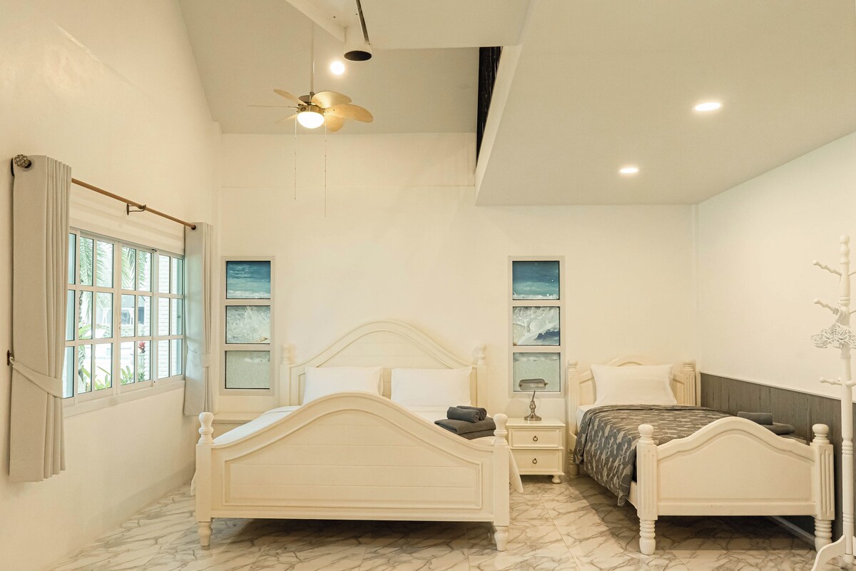 Une chambre avec deux lits, un ventilateur de plafond et une fenêtre avec des rideaux.
