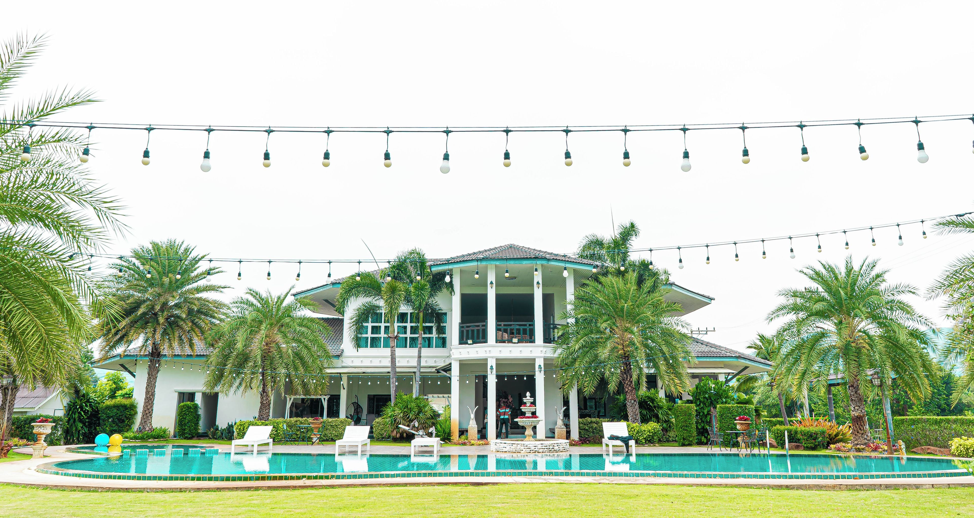 A two-story house with a swimming pool, surrounded by palm trees and a string of lights.