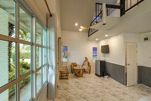 A spacious room with a large window, a ceiling fan, a dining table with chairs, and a television. - Saithong Resort (Pranburi)