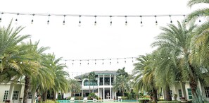 A building with a pool, palm trees, and string lights. - Saithong Resort (Pranburi)