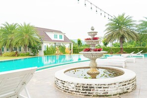 A swimming pool with a fountain, lounge chairs, and a house in the background. - Saithong Resort (Pranburi)