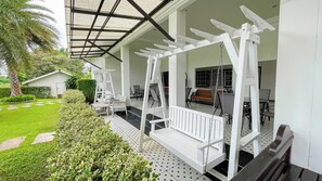 A covered outdoor seating area with white furniture, a pergola, and a well-maintained garden. - Saithong Resort (Pranburi)