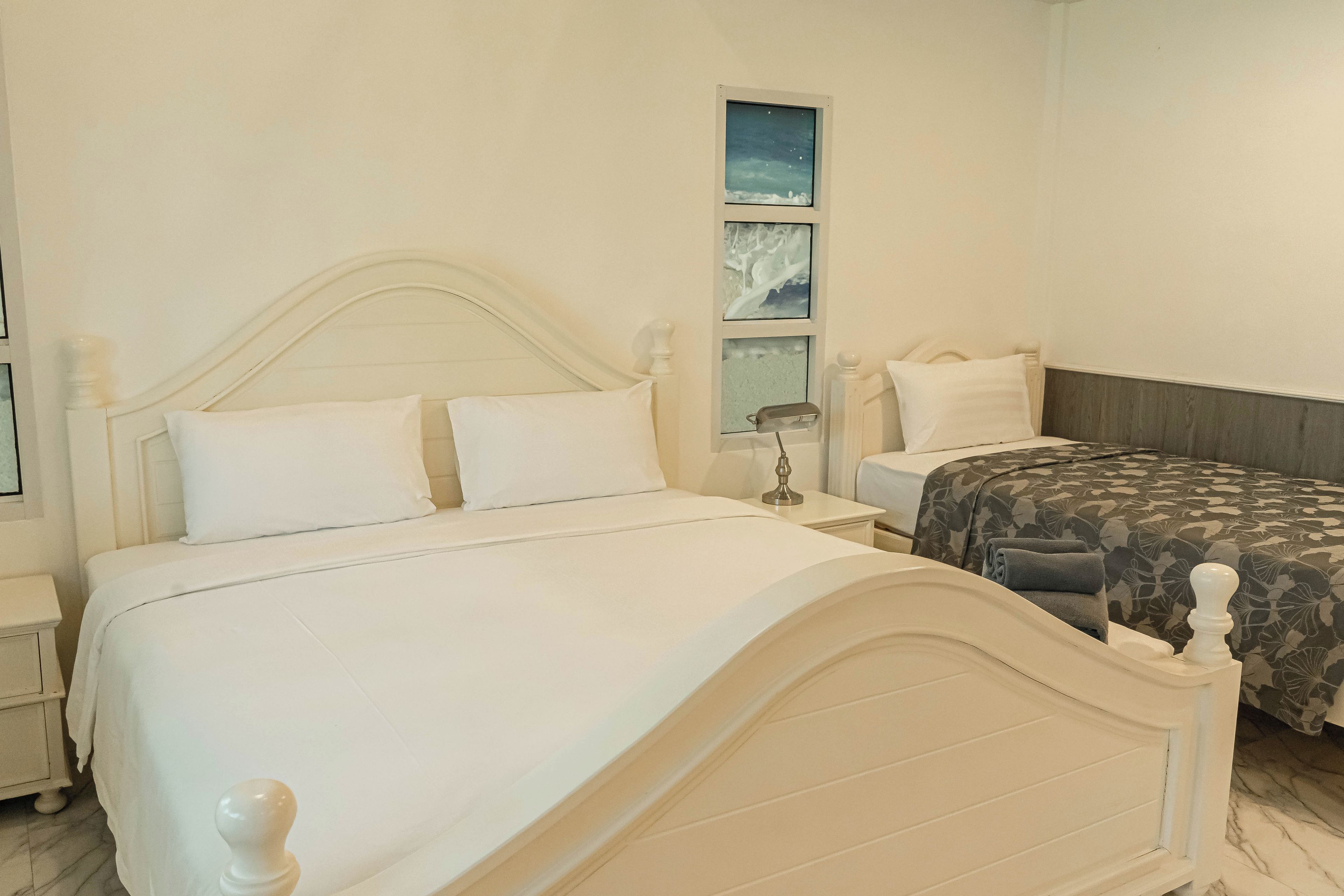 A bedroom with a white bed, a nightstand, a bedside table, and a wall-mounted shelf with framed pictures.