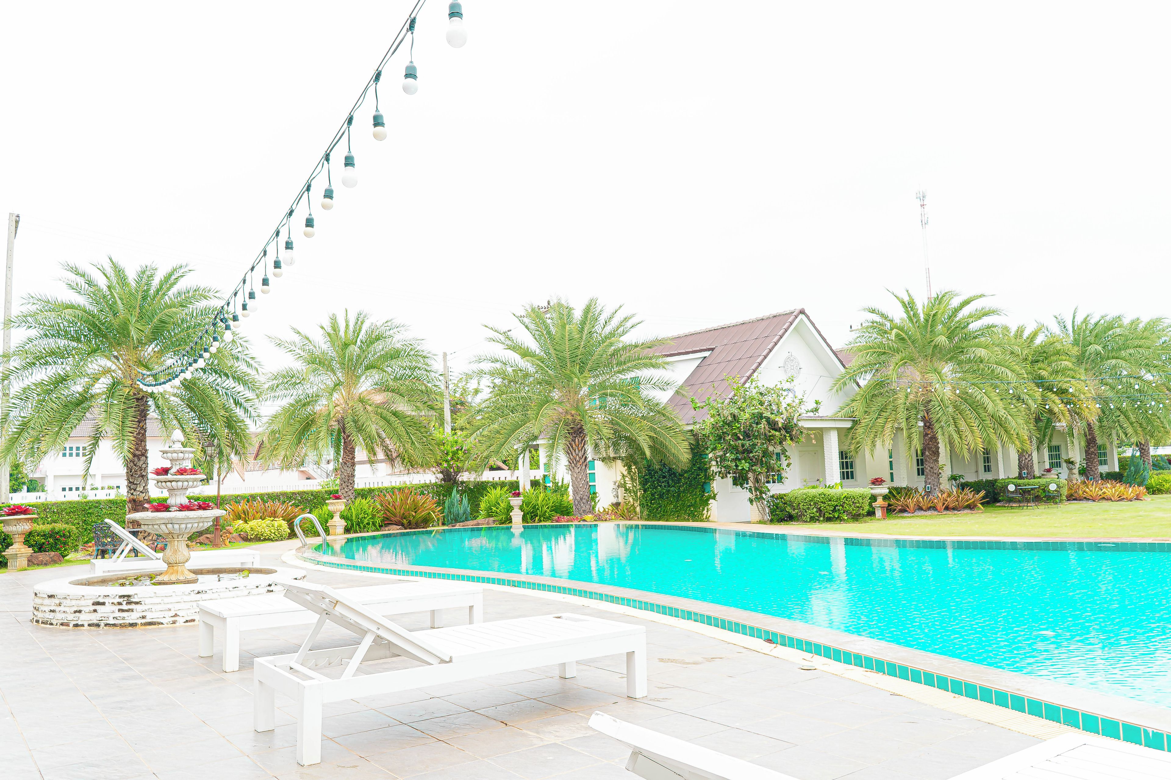 A swimming pool with lounge chairs, palm trees, and a building in the background.