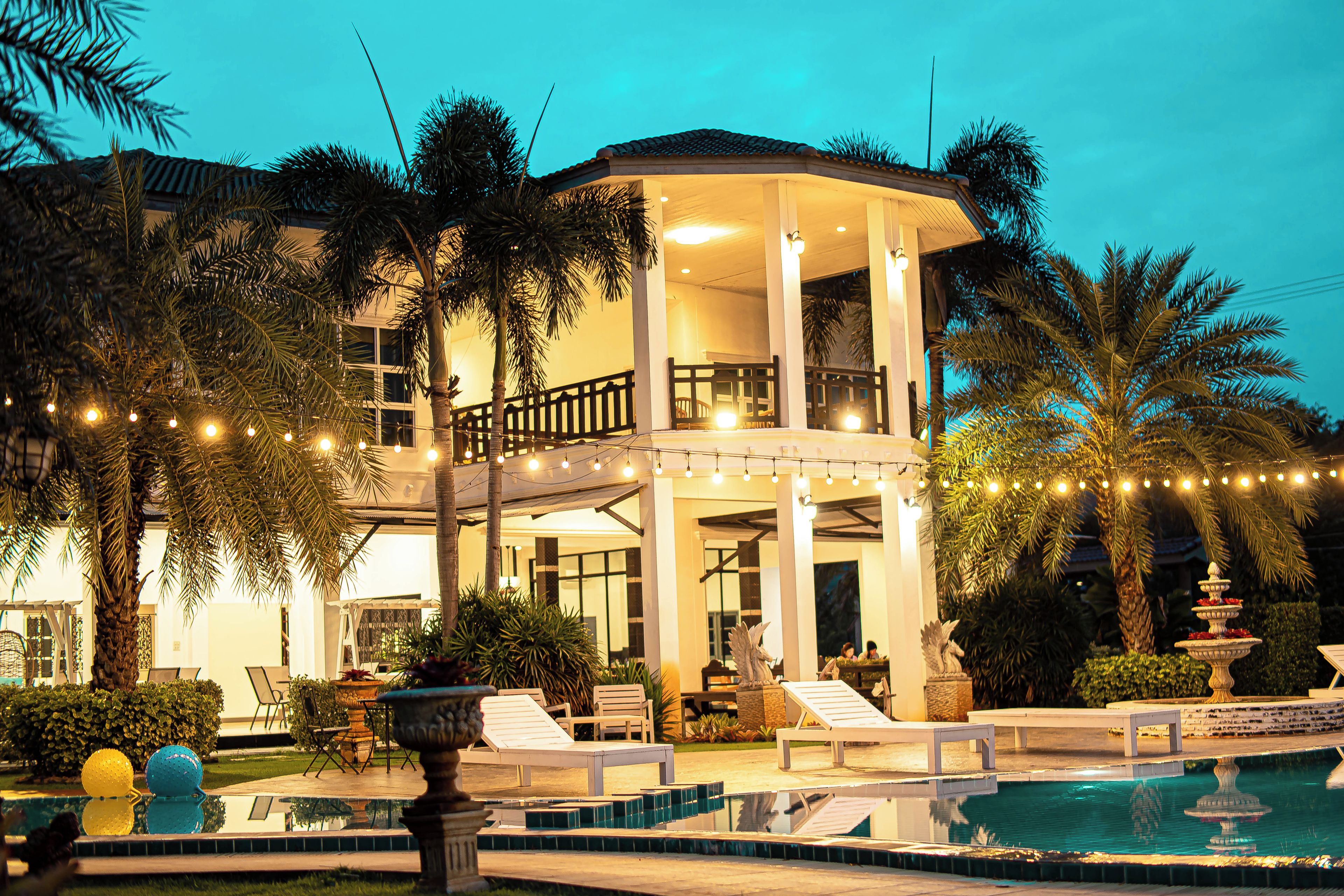 A two-story building with a covered outdoor area, a swimming pool, and palm trees.