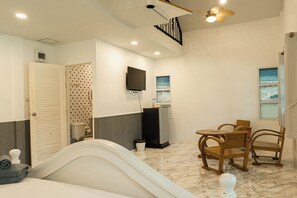 A hotel room with a bed, a desk with a computer, a TV mounted on the wall, and a ceiling fan. - Saithong Resort (Pranburi)