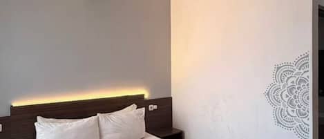 A modern hotel room with a bed, bedside table, and a decorative wall design.