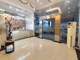 Zona de recepción de un hotel con mostrador, planta en maceta, reloj de pared y un equipo de aire acondicionado grande.