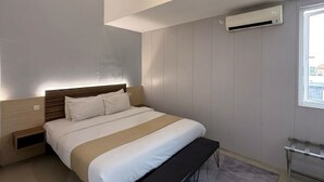 A modern bedroom with a bed, bedside tables, a bench, and an air conditioning unit. - De La Charis Hotel (Tulungagung)