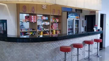 A bar area with a tiled counter, shelves stocked with snacks, and three red bar stools.