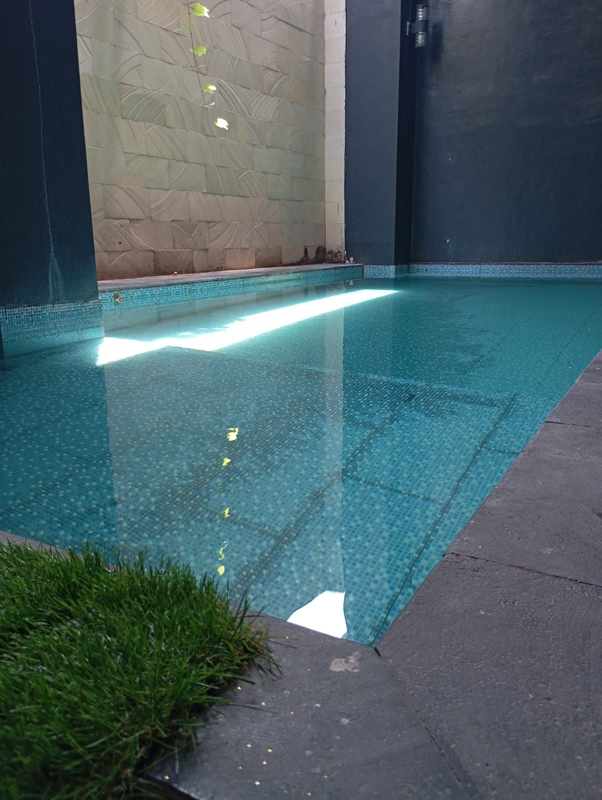 Una piscina con borde de azulejos, rodeada de muros con un diseño texturizado.
