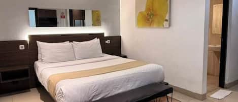 A modern hotel room with a large bed, a nightstand, a wall-mounted mirror, and a painting.