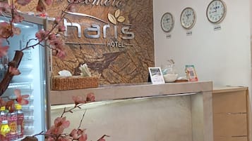 En hotellreception med en välkomstskylt, klockor som visar olika tidszoner och ett dekorativt träd med rosa blommor.