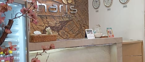 A hotel reception desk with a welcome sign, clocks displaying different time zones, and a decorative tree with pink flowers.