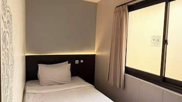 A single bed with a headboard, a window with curtains, and a wall with a decorative pattern.