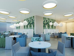 Un restaurante moderno con mesas redondas, asientos en tonos azul y gris, y una pared decorada con motivos de hojas tropicales.