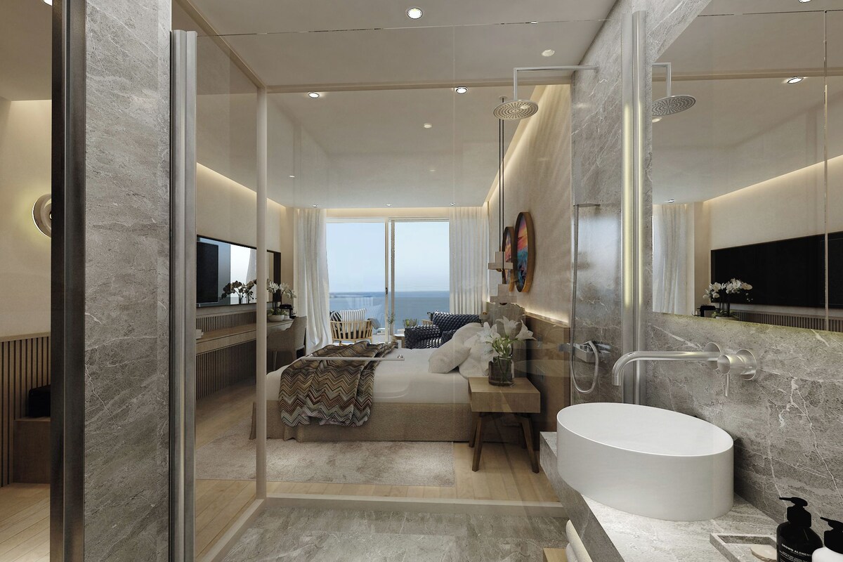 A modern bathroom with a large bathtub, a glass-enclosed shower, and a view of the sea.