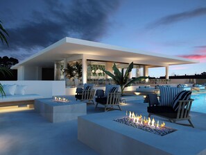 A modern outdoor lounge area with seating, a fire feature, and a pool. - Infinity Napa Hotel (Ayia Napa)