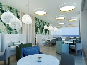 A modern lounge area with seating, a table with a candle, and a view of the ocean. - Infinity Napa Hotel (Ayia Napa)