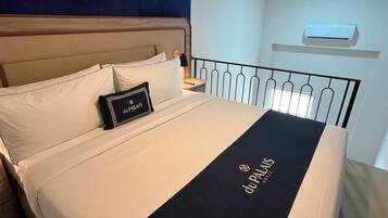 Una habitación de hotel con una cama, una mesita de noche, un aire acondicionado de pared y una lámpara en el techo.