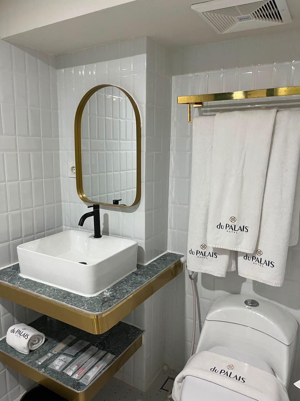 Une salle de bain avec un lavabo blanc, un miroir à cadre doré et un porte-serviettes avec des serviettes blanches.