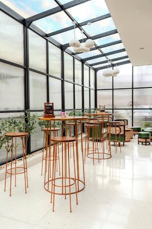 Amplio espacio interior con techo alto y ventanas grandes, con varias mesas y sillas dispuestas para sentarse.