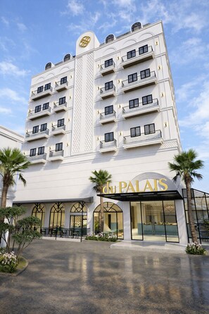 A multi-story hotel with balconies, a prominent entrance, and palm trees. - du Palais Hotel (Jambi)